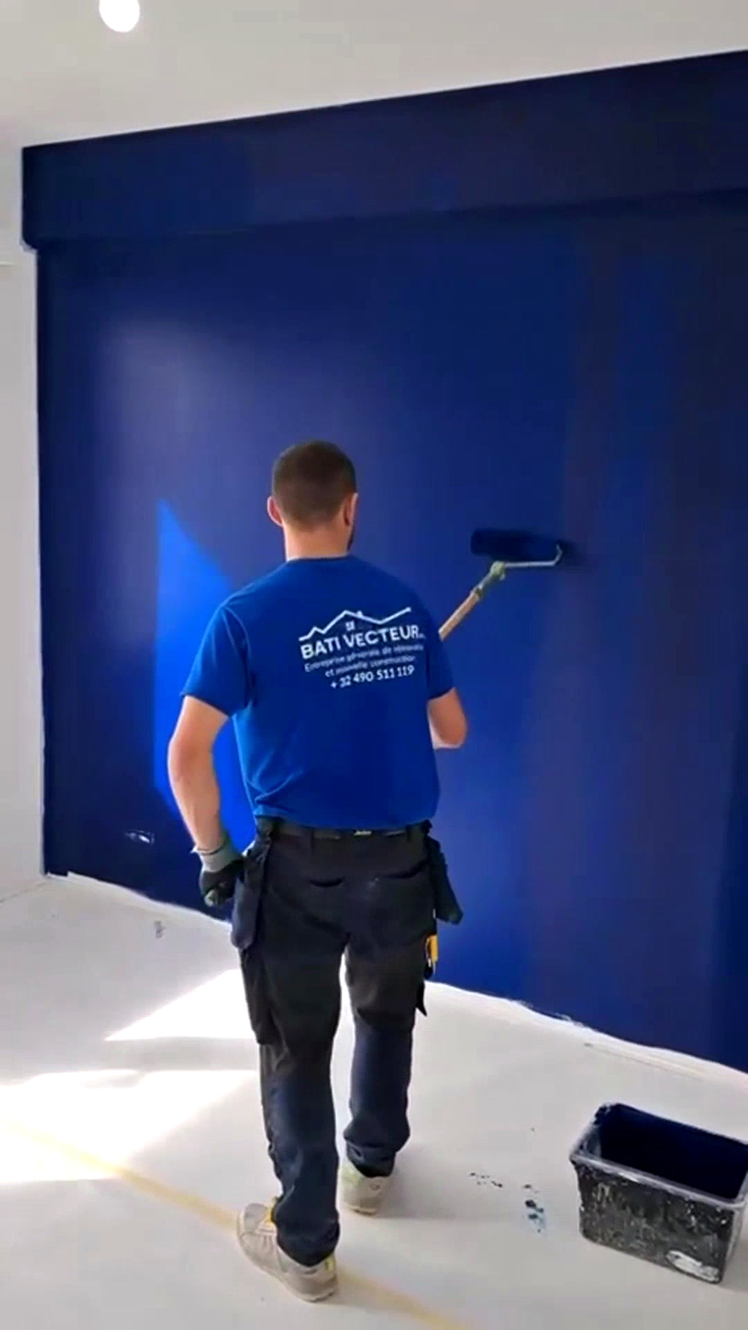 Un membre de l'équipe BATI VECTEUR peint un mur bleu au rouleau