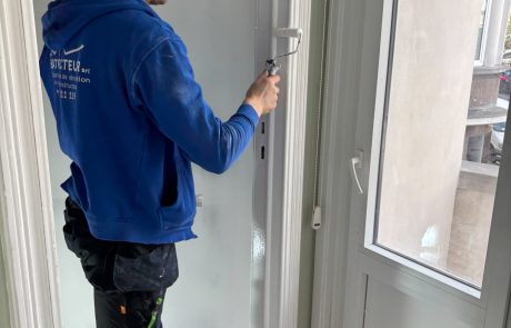 Un peintre de la société Bati Vecteur peint un cadre de porte blanc au rouleau