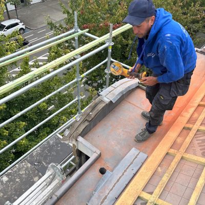 Finition en ardoise installée manuellement autour d’un élément décoratif de façade pour assurer l’étanchéité