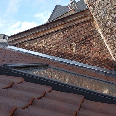 Toiture en tuiles entièrement rénovée avec fenêtre de toit et solins métalliques contre un mur en briques