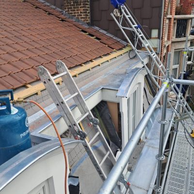 Vue d’une toiture en tuiles rénovée avec acrotère et chéneau en zinc, accessible par échafaudage